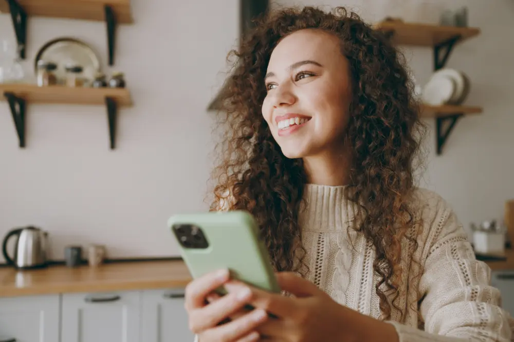 Happy woman holding her mobile phone, taking part in an online counselling session at home.