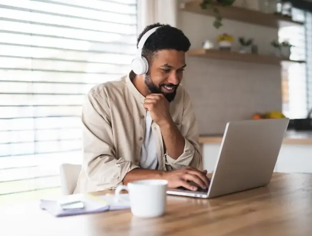 Smiling man wearing headphones, taking part in an online counselling session on his laptop at home.
